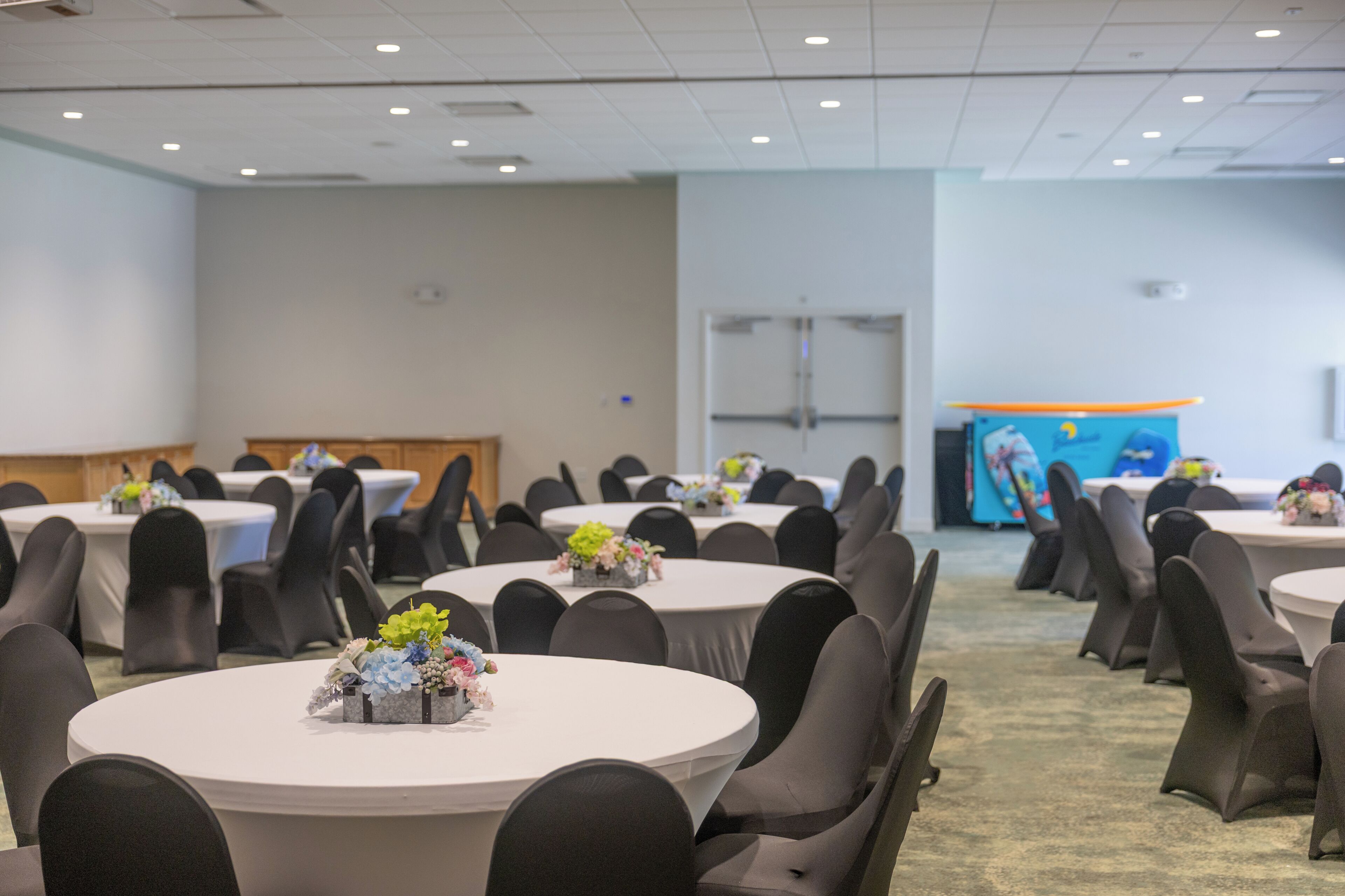 Un salón de conferencias con mesas redondas, sillas negras y centros de mesa con flores.