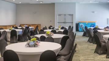Un salón de conferencias con mesas redondas, sillas negras y centros de mesa con flores.
