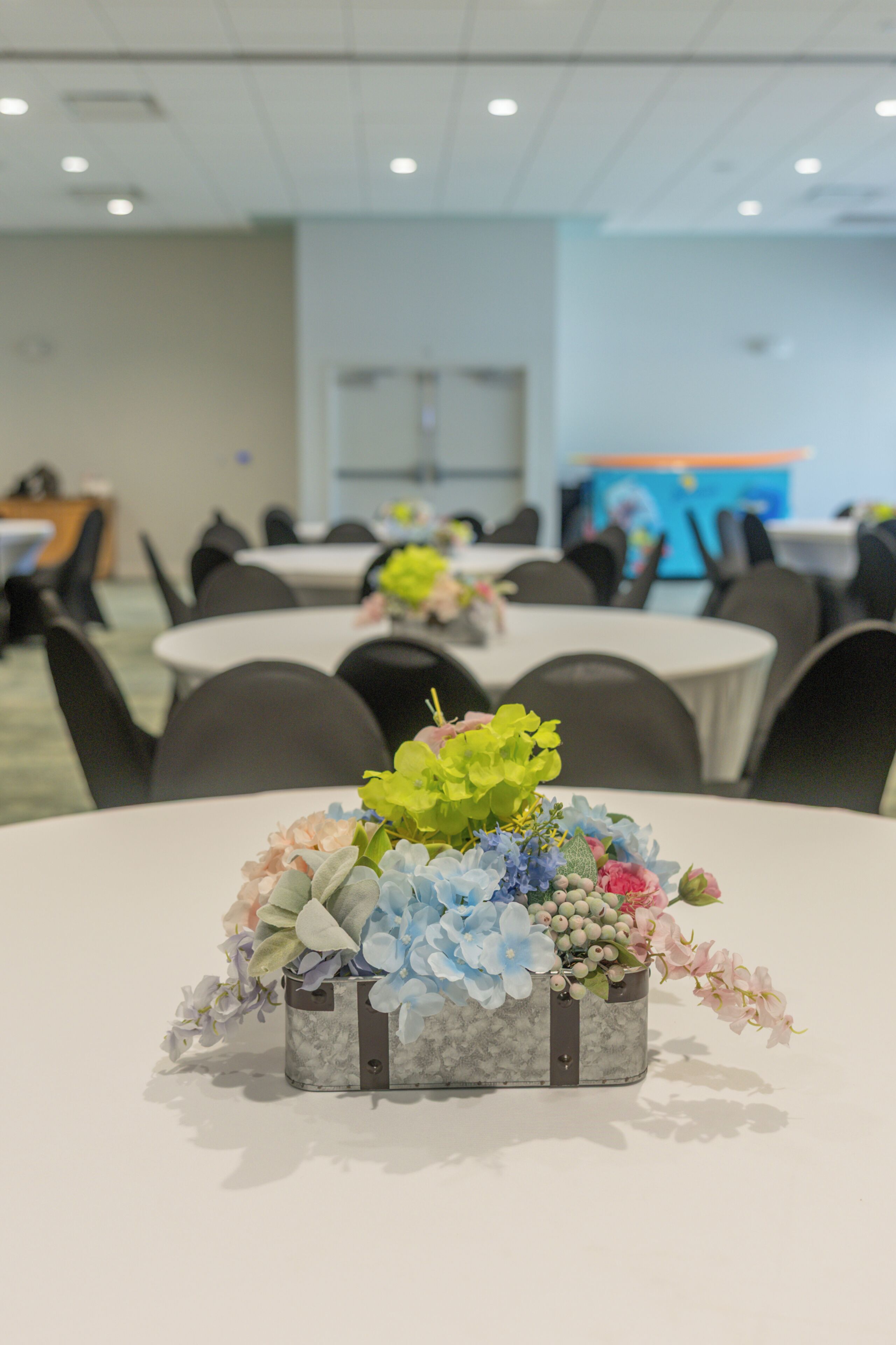 Ein Konferenzraum mit runden Tischen, Stühlen und einer floralen Tischdekoration auf einem Tisch.