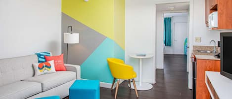 A modern living room with a sofa, colorful cushions, a bright wall, and a kitchen area in the background.