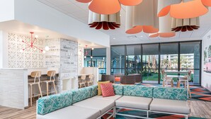 A modern lounge area with a sectional sofa, a bar area, and a view of the outdoors. - Beachside Hotel & Suites Cocoa Beach - Port Canaveral (Cocoa Beach)