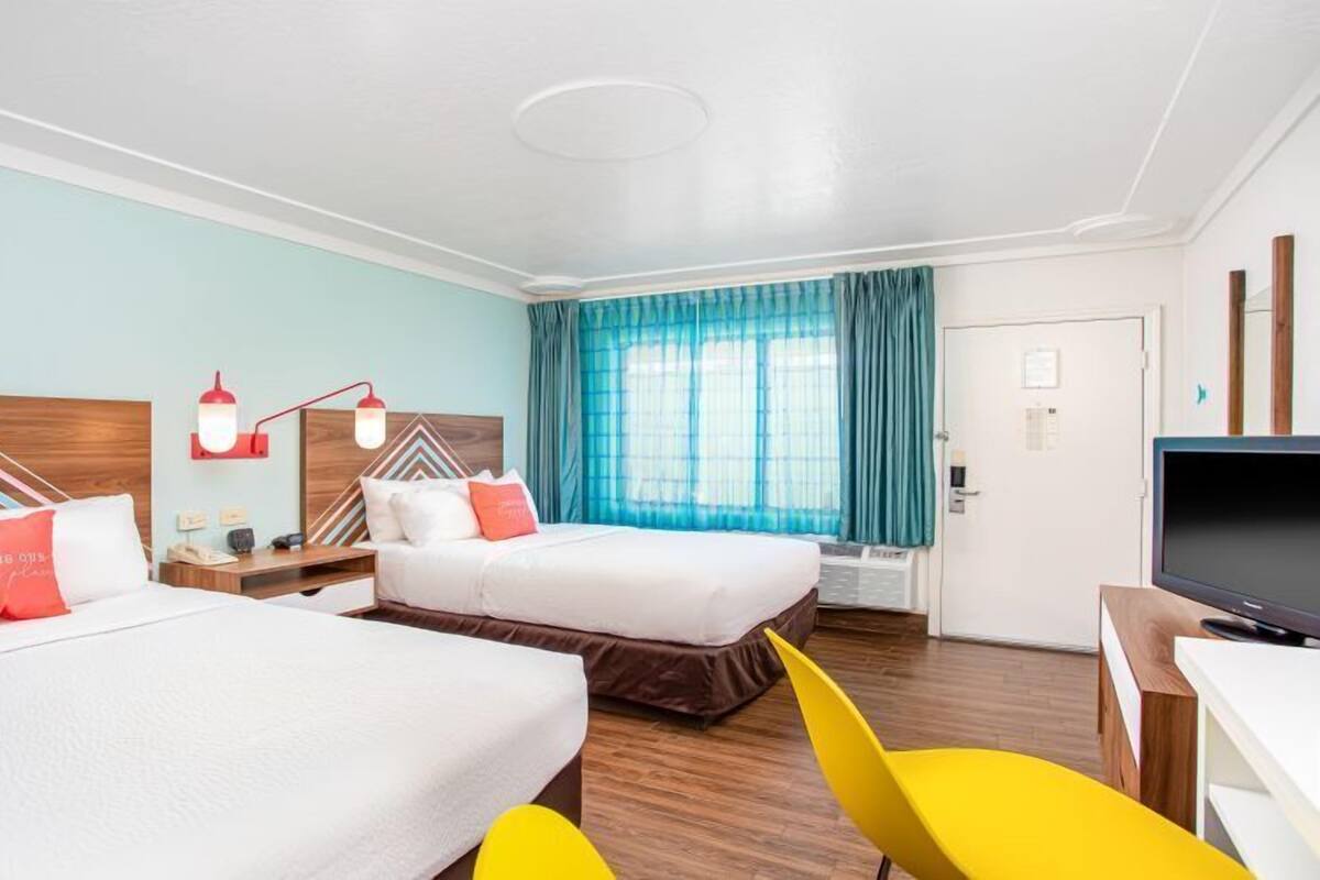 A hotel room with two beds, a TV, a desk, and a chair.