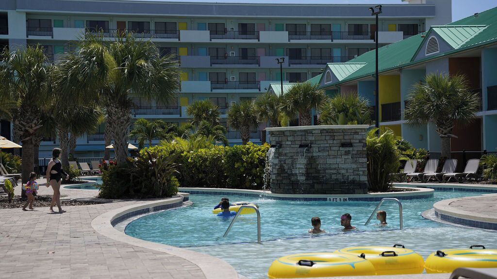 Un espace piscine d’hôtel doté de plusieurs niveaux de balcons, de palmiers et de chaises longues.