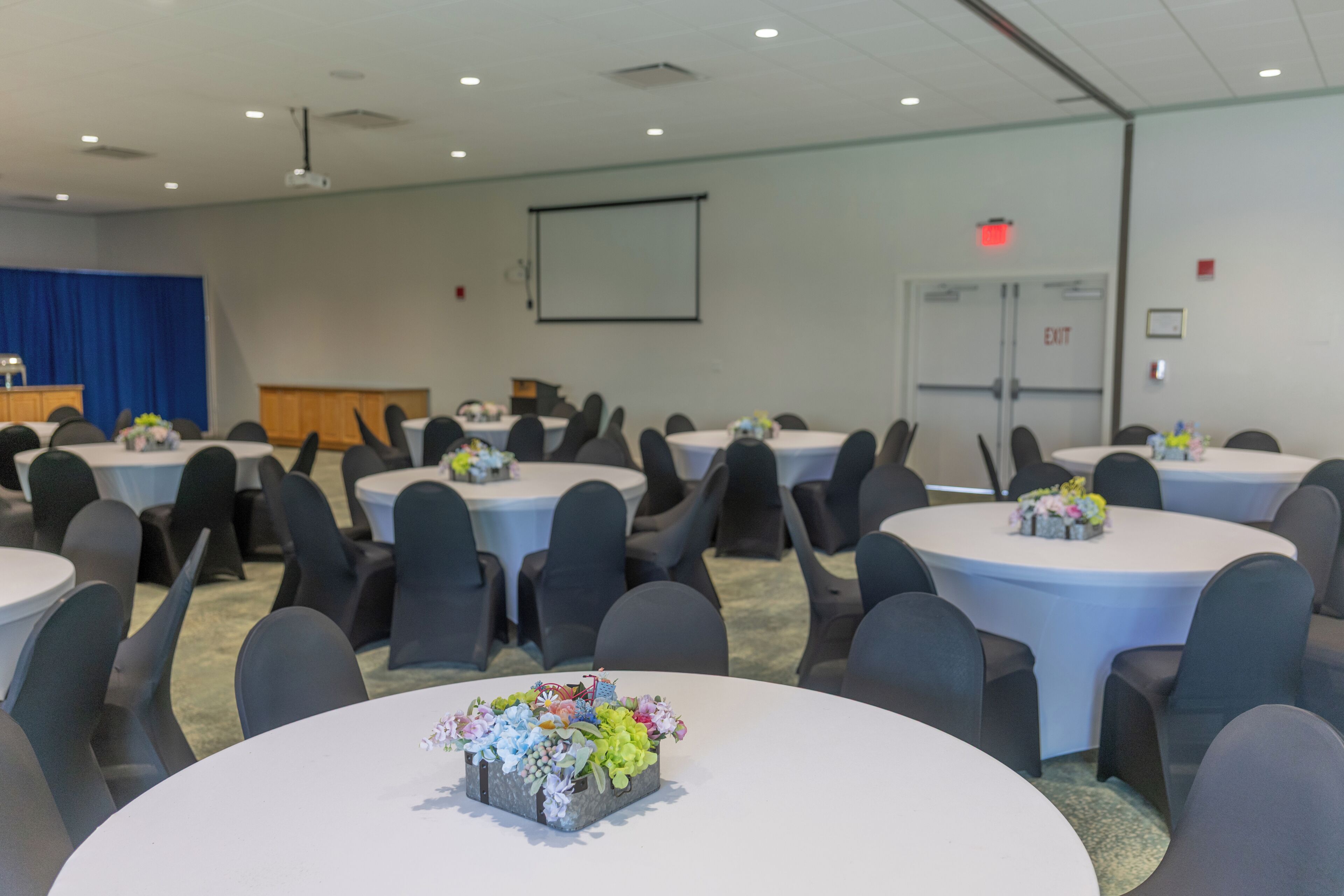 A conference room with round tables, chairs, and a projector screen.