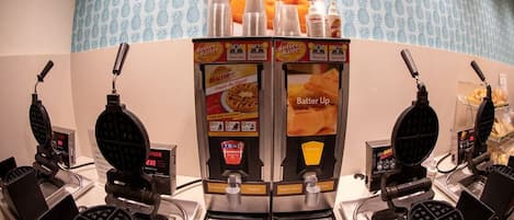 A waffle station with multiple waffle makers, a display of waffles, and a sign for 'Batter Up'.