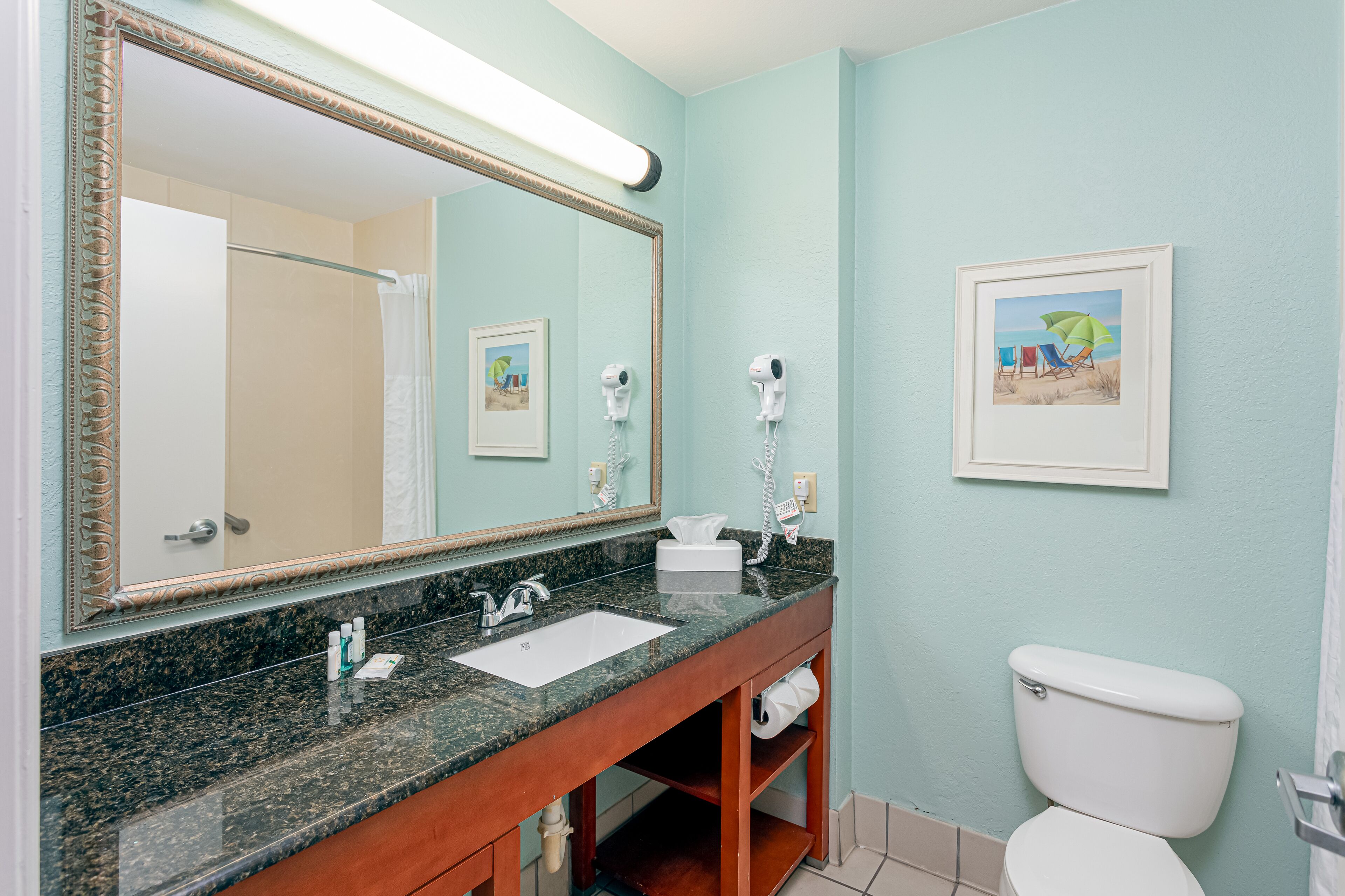 A bathroom with a marble sink, a large mirror, a toilet, and a framed beach scene on the wall.