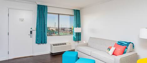 Een moderne woonkamer met een bank, poefs, een lamp en uitzicht op een tennisbaan.