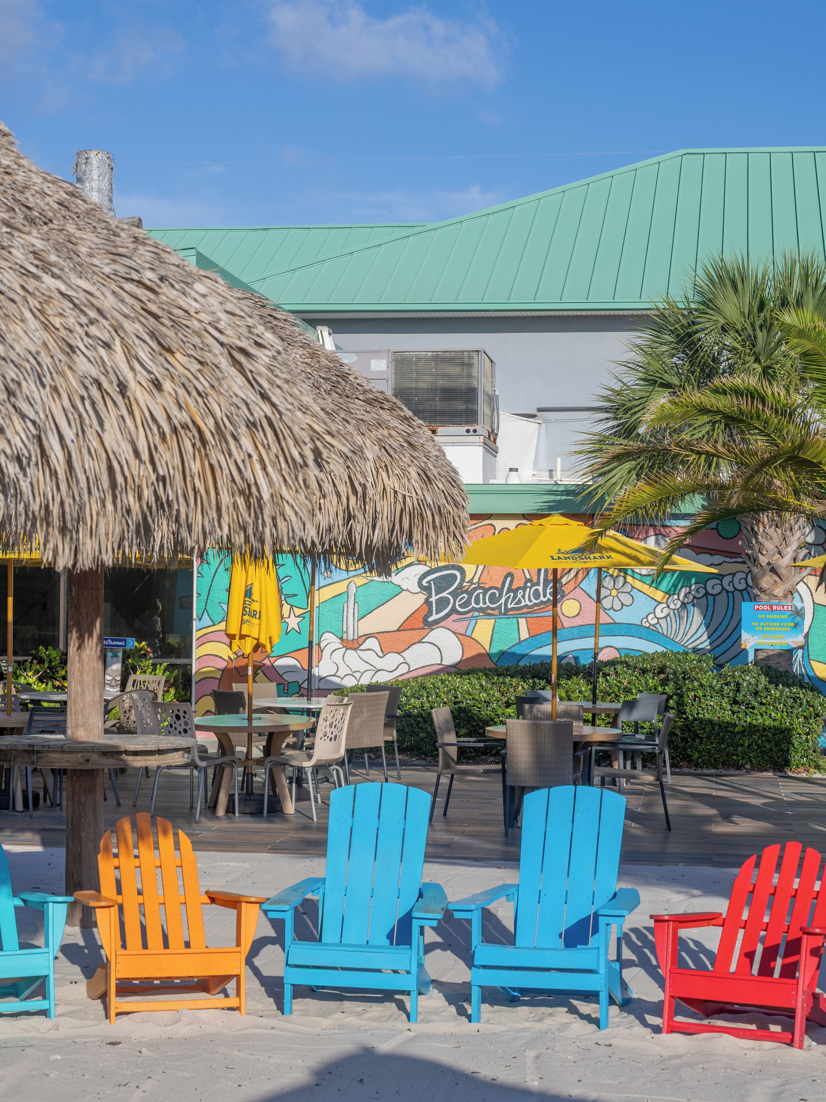 Un restaurante junto a la playa con terraza, un mural y una estructura de techo de paja.