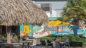 Un restaurante junto a la playa con terraza, un mural y una estructura de techo de paja.