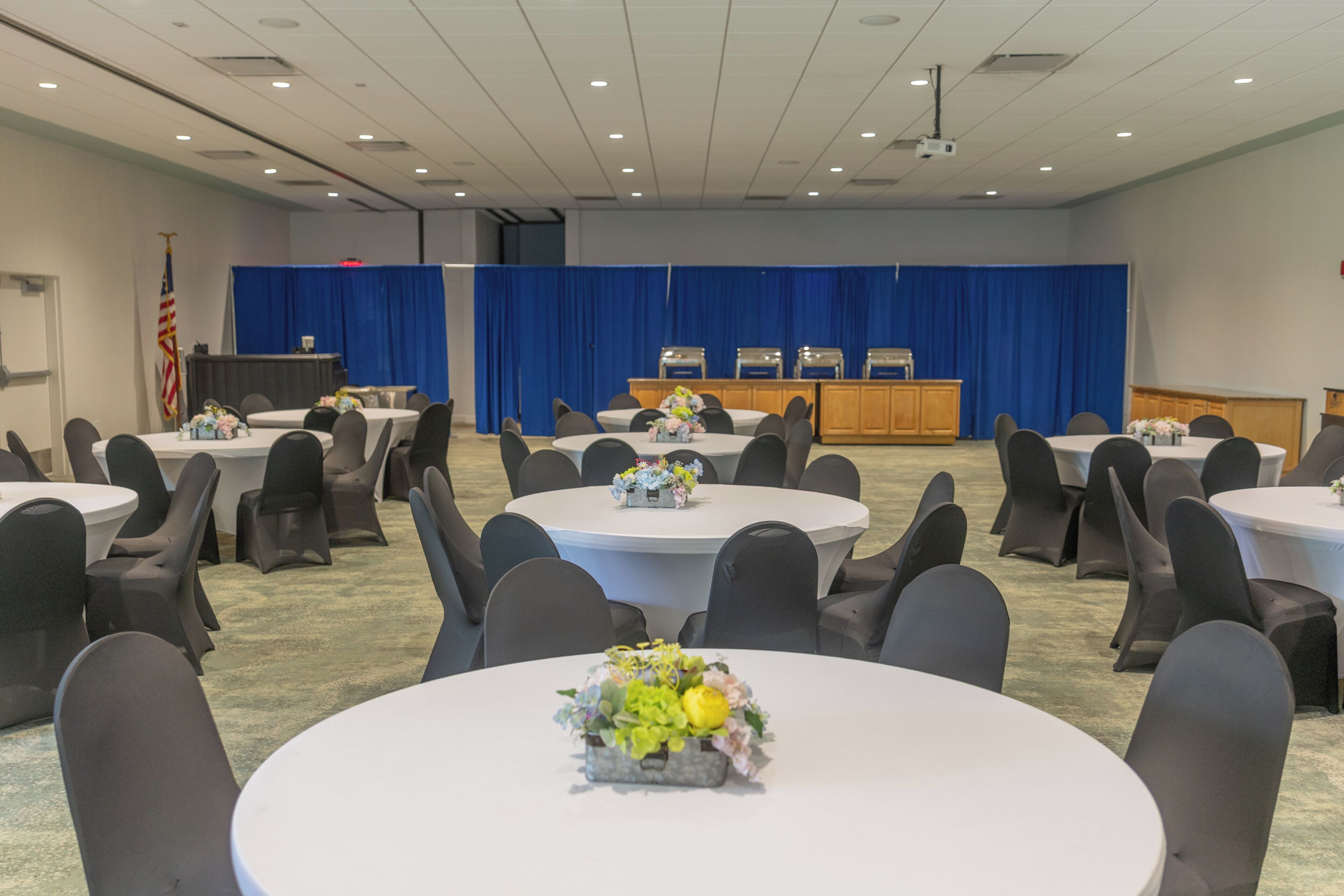 A conference room with round tables, chairs, a podium, and a blue curtain backdrop.