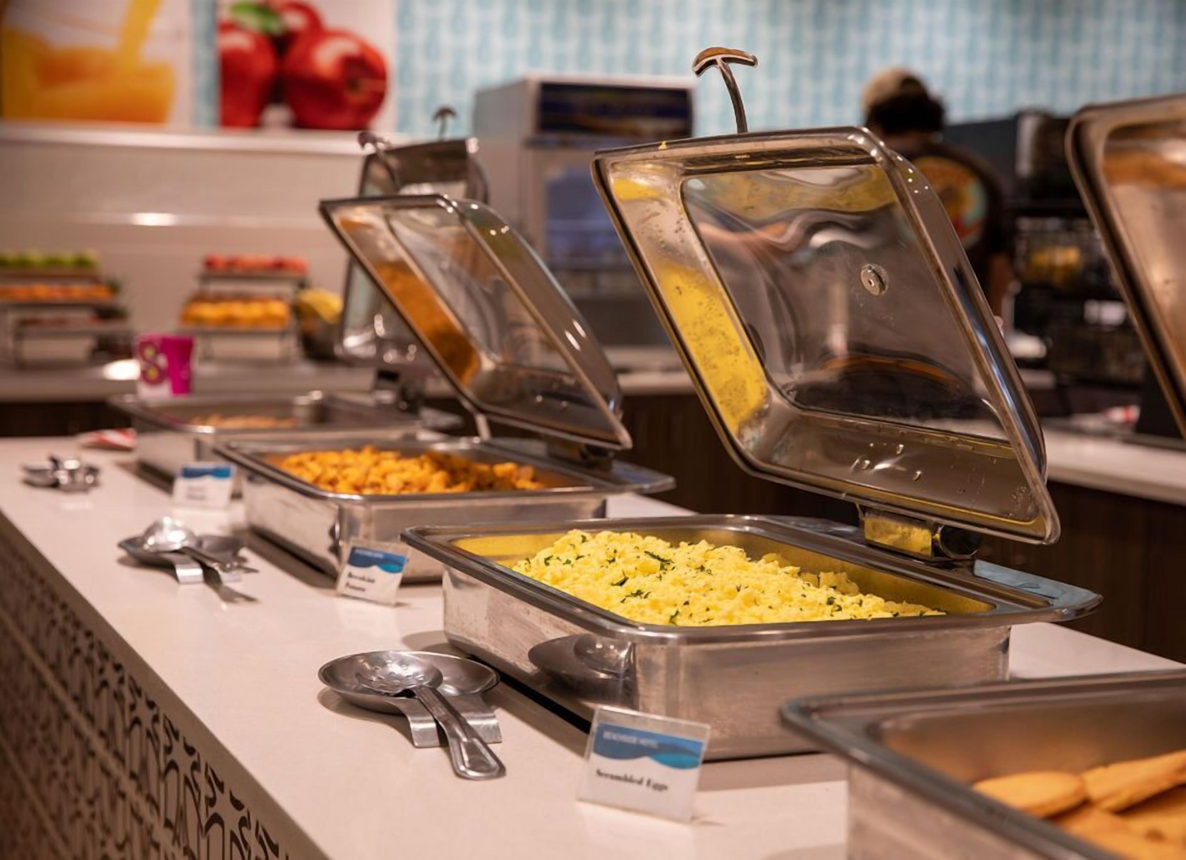 A buffet with various food options, including scrambled eggs and other dishes, with serving utensils and labels.