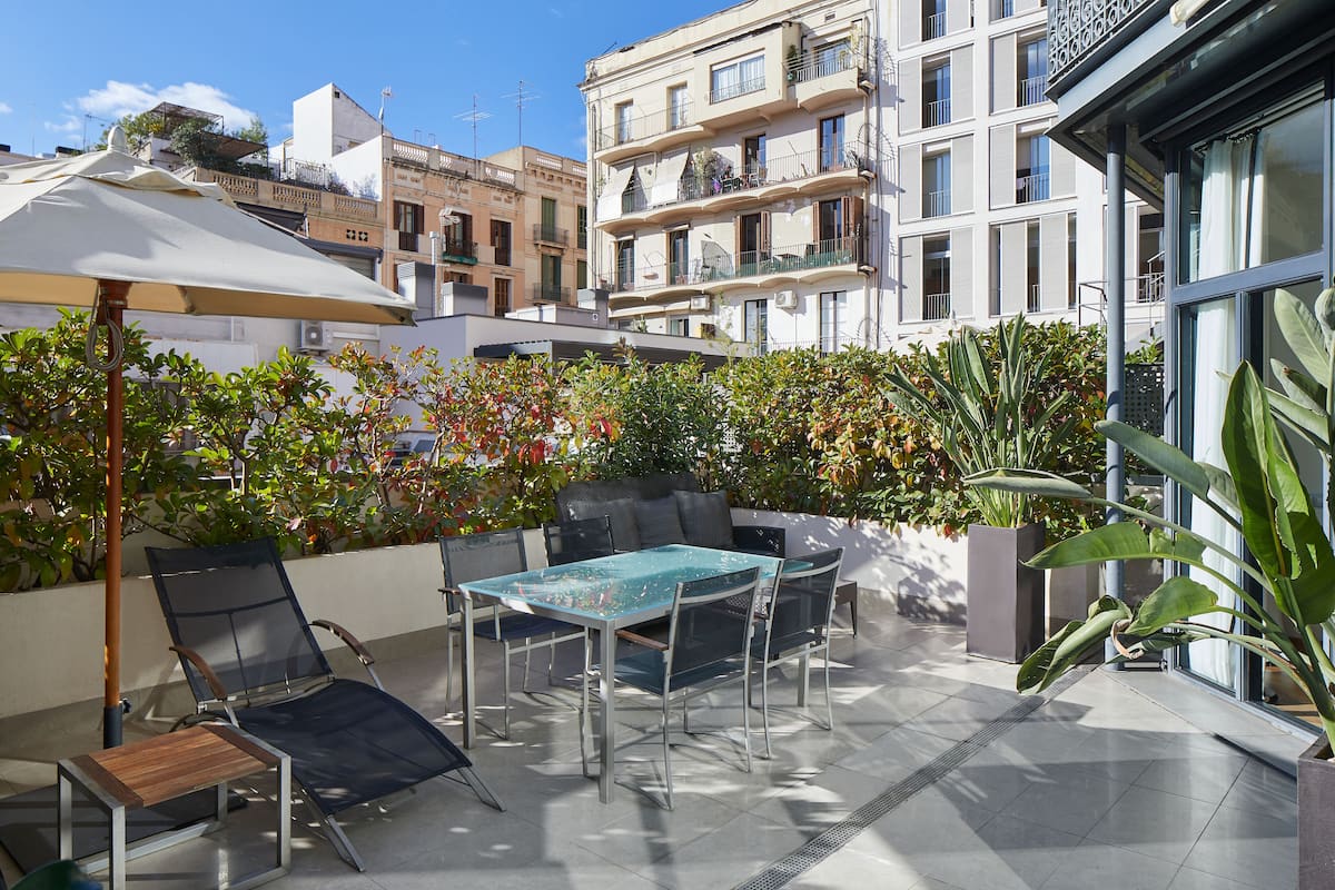 An outdoor patio area with a table and chairs, surrounded by plants and a view of a residential building.