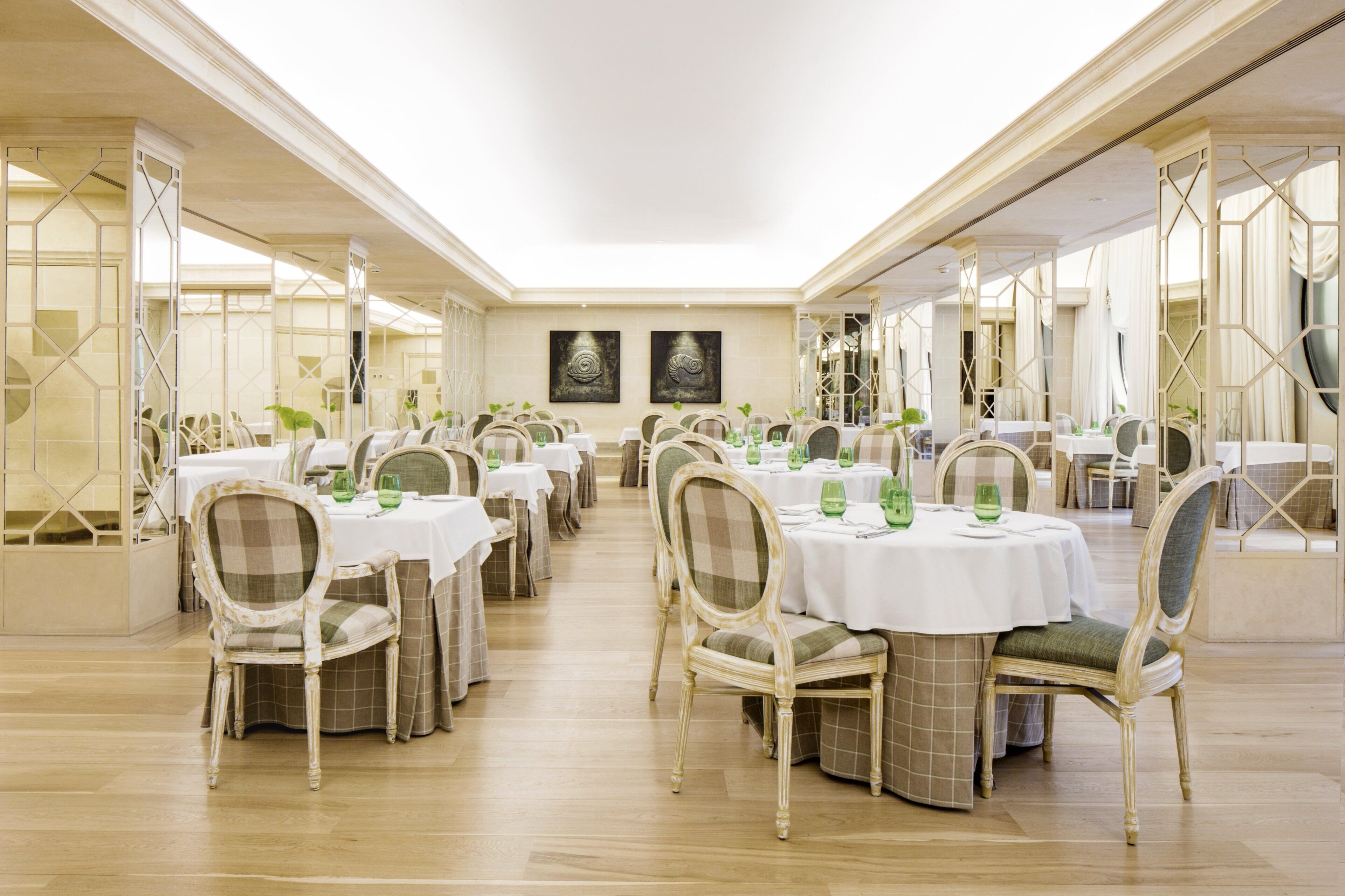Un comedor espacioso con varias mesas redondas, cada una con sillas y copas de vidrio verde.