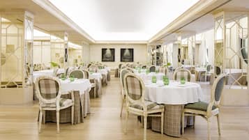 Un comedor espacioso con varias mesas redondas, cada una con sillas y copas de vidrio verde.