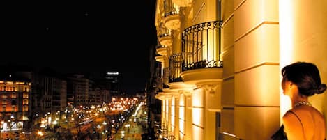 A night view of a city street with illuminated buildings and a balcony overlooking the scene.