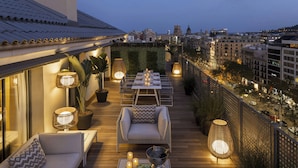 Eine Dachterrasse mit Esstisch für sechs Personen, umgeben von Korbmöbeln, Blumentöpfen und stimmungsvoller Beleuchtung.