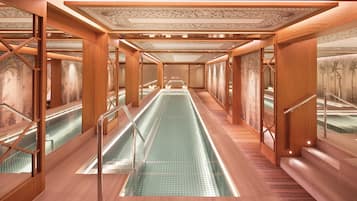 Une longue et étroite zone de piscine dotée d’un plancher en verre, de murs en bois et d’un plafond orné de motifs complexes.