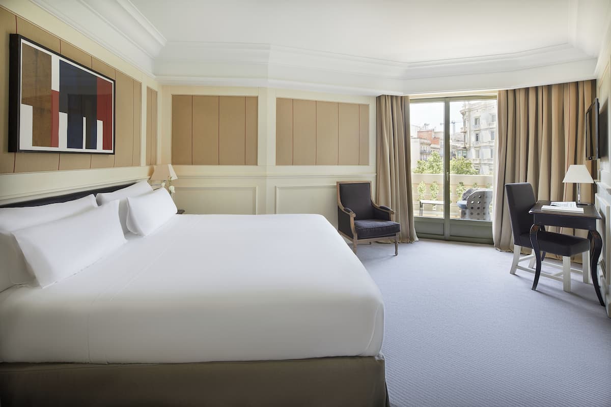 A hotel room with a large bed, a desk, a chair, and a TV mounted on the wall.