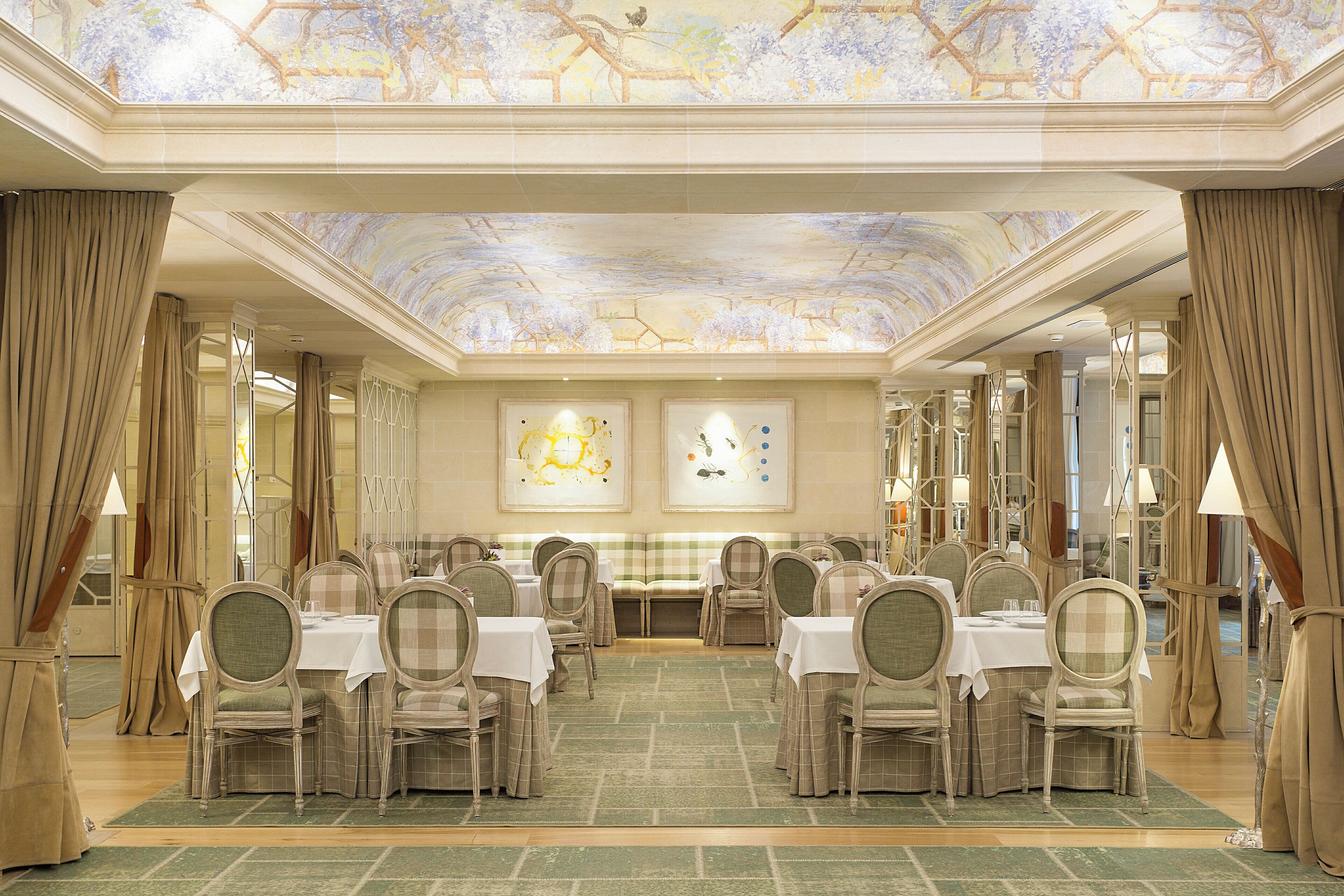 Un salón de banquetes con varias mesas y sillas, una alfombra verde y un techo decorado con un mural floral.