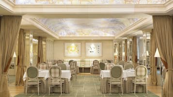Un salón de banquetes con varias mesas y sillas, una alfombra verde y un techo decorado con un mural floral.