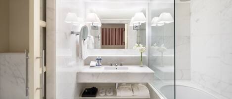 A modern bathroom with a glass shower enclosure, a marble sink, and a vanity with a mirror and two wall-mounted lamps.
