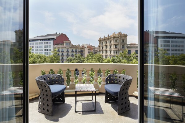 Un balcón con dos sillas estampadas y una pequeña mesa, con vistas a un paisaje urbano con edificios históricos.