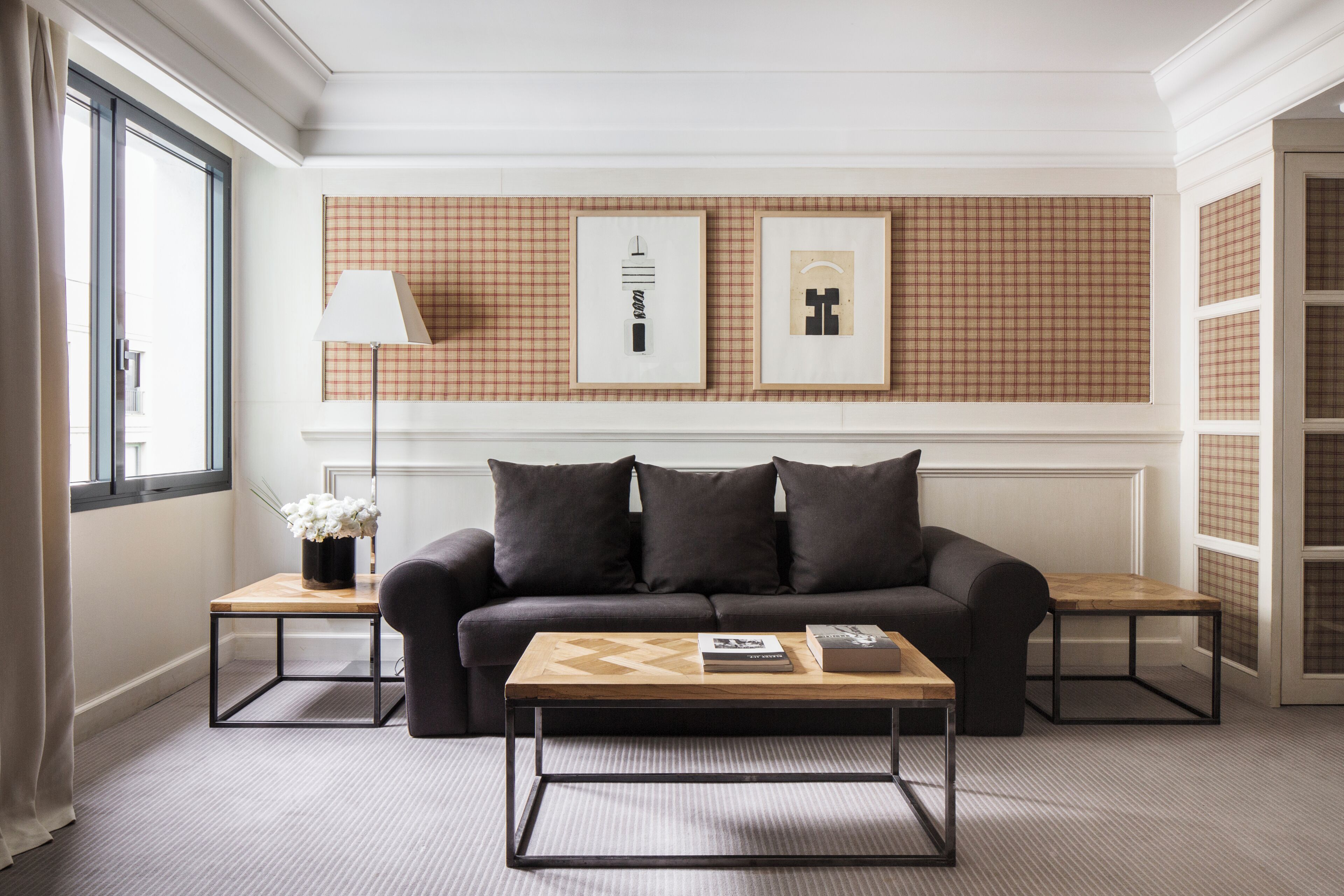 A modern living room with a sofa, coffee table, and two side tables. There are framed pictures on the wall, a floor lamp, and a window with curtains.