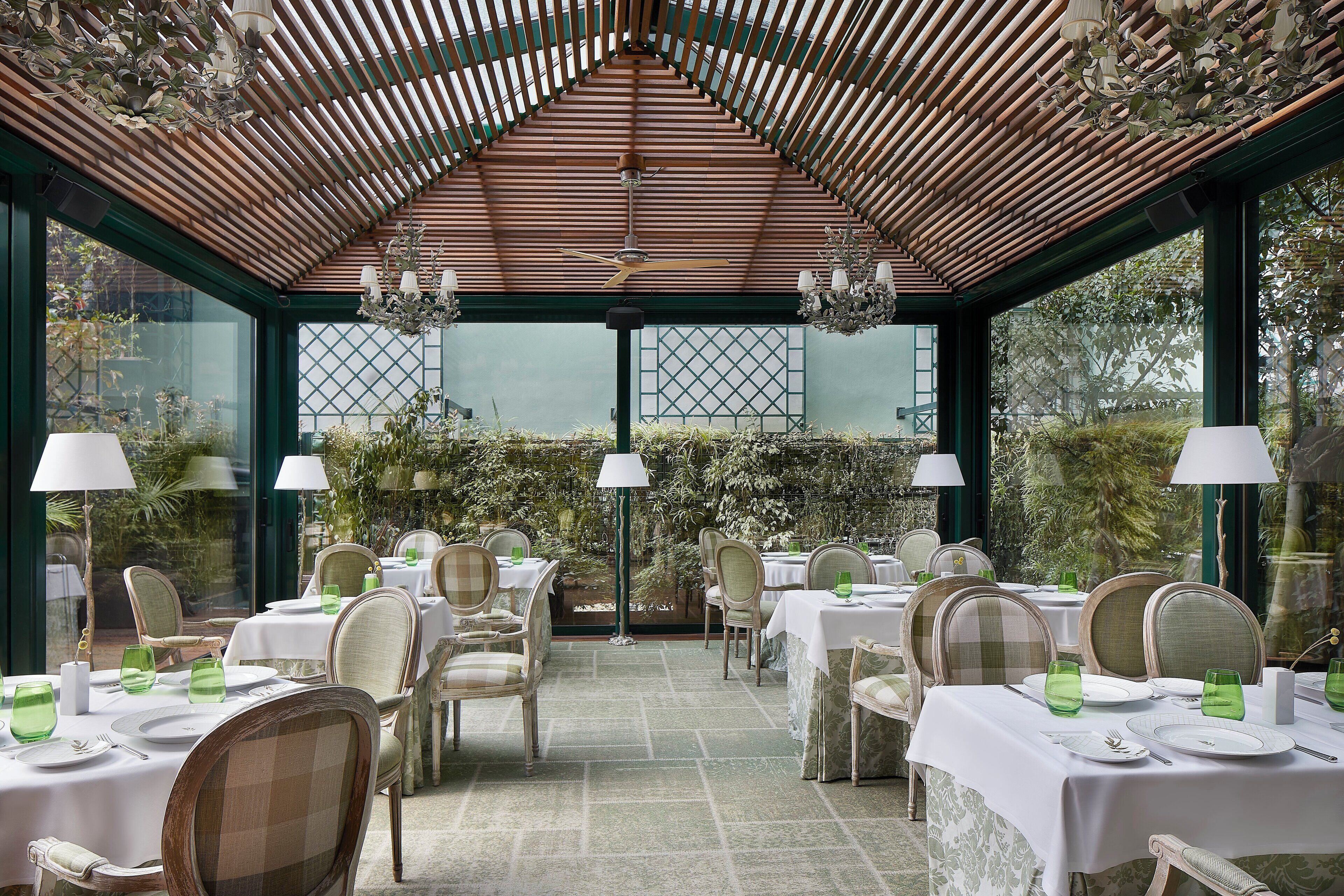 A restaurant with tables set for dining, featuring a wooden ceiling and large windows.