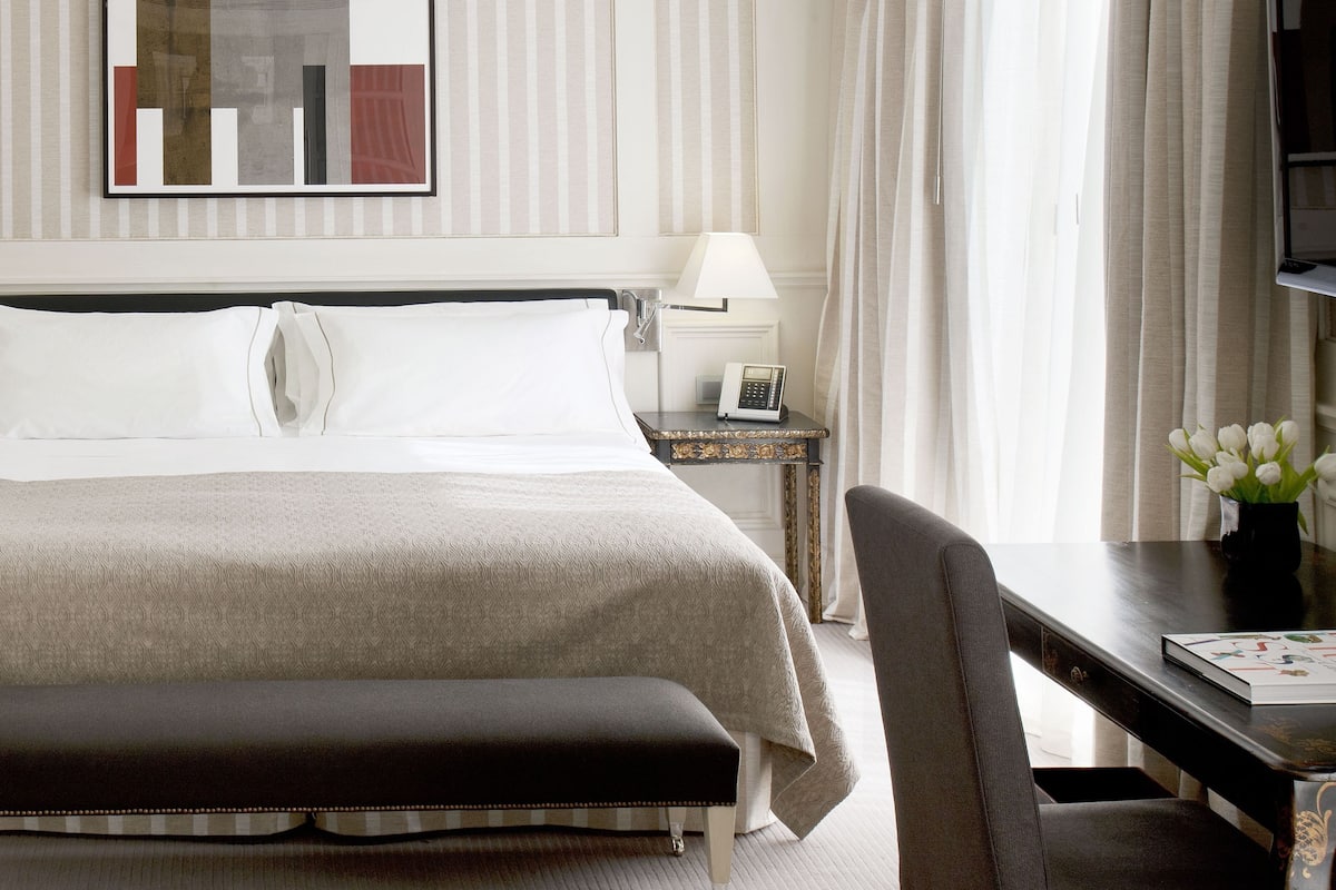 A hotel room with a large bed, a desk with a lamp, a chair, and a television.
