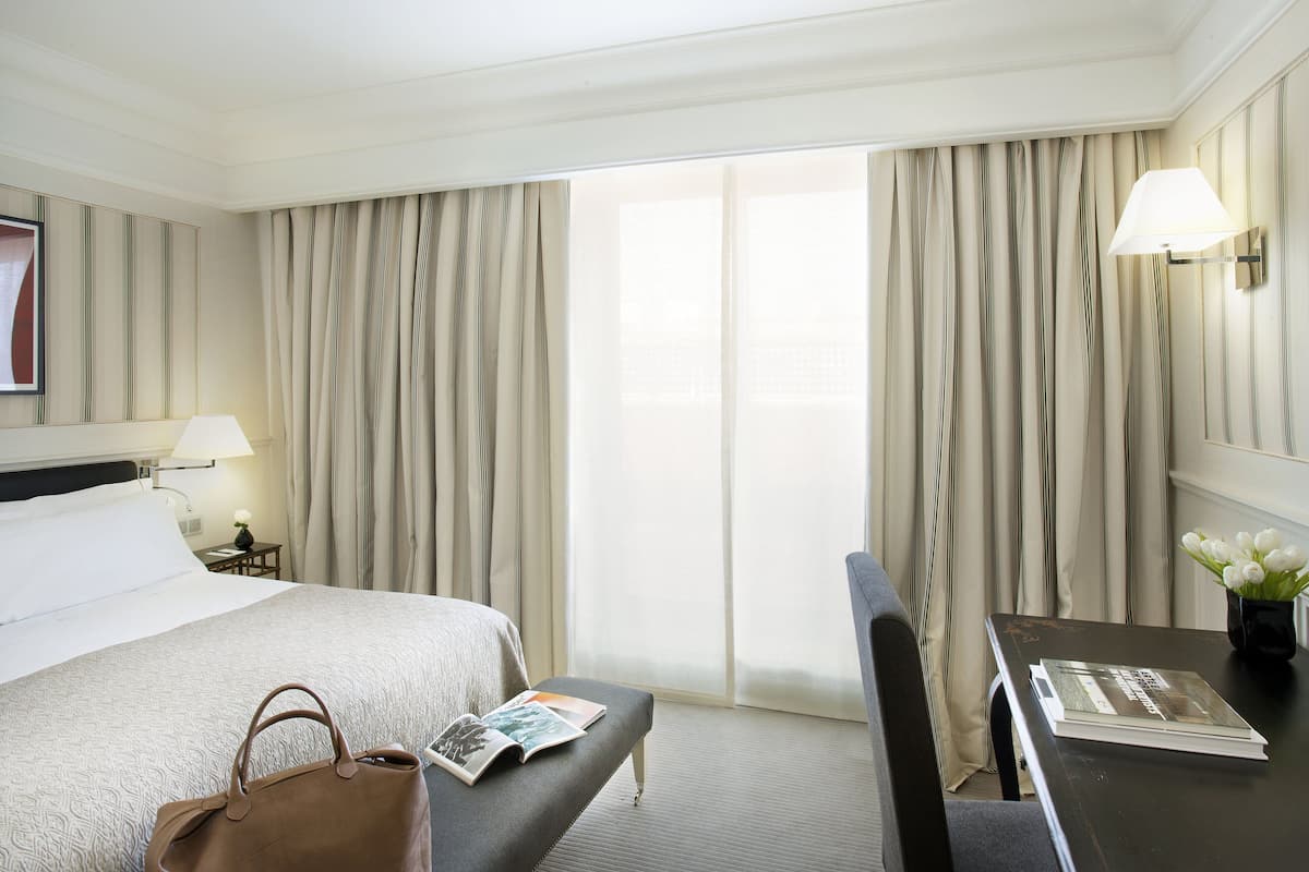 A hotel room with a bed, bedside table, lamp, and a view through the window.