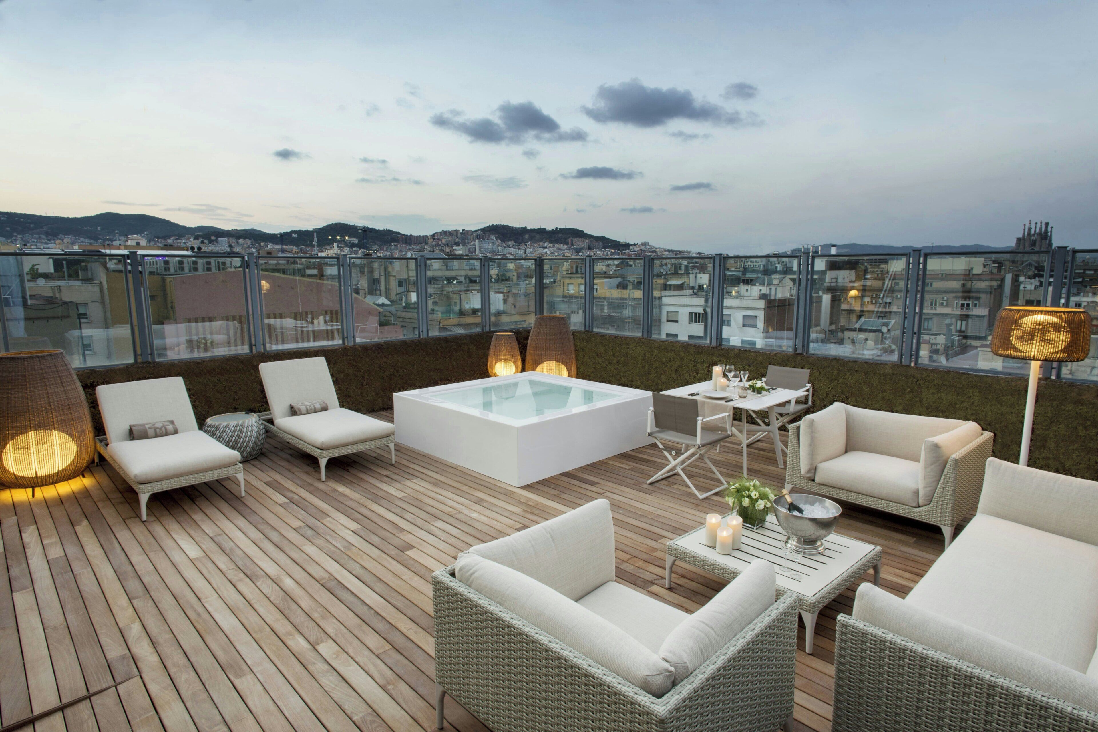 A rooftop terrace with a glass-enclosed pool, lounge chairs, and a view of the cityscape.