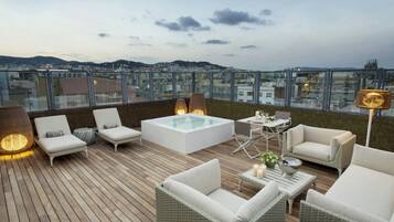 A rooftop terrace with a glass-enclosed pool, lounge chairs, and a view of the cityscape.