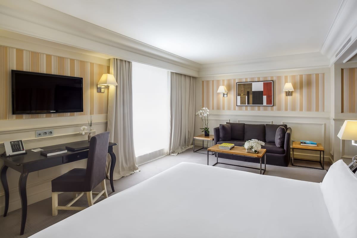 A hotel room with a large bed, a desk with a computer, a sofa, and a TV.