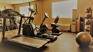 Un gimnasio con cintas de correr, bicicletas estáticas y un espejo grande.