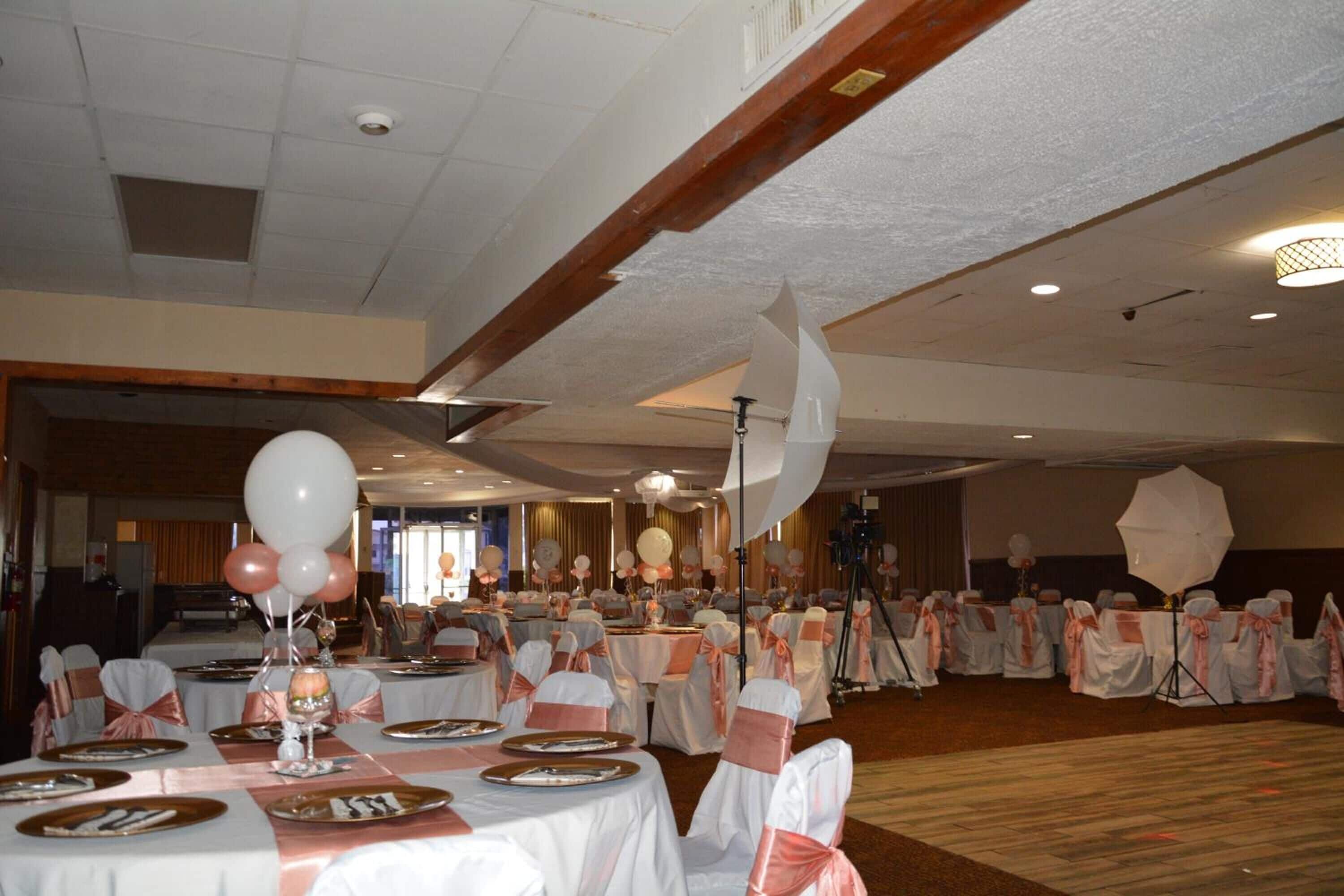 Un salón de banquetes con mesas redondas, manteles blancos y cintas rosas.