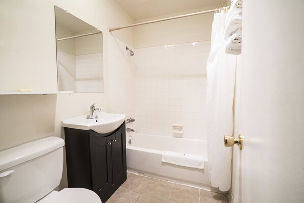 A bathroom with a toilet, sink, mirror, and bathtub.