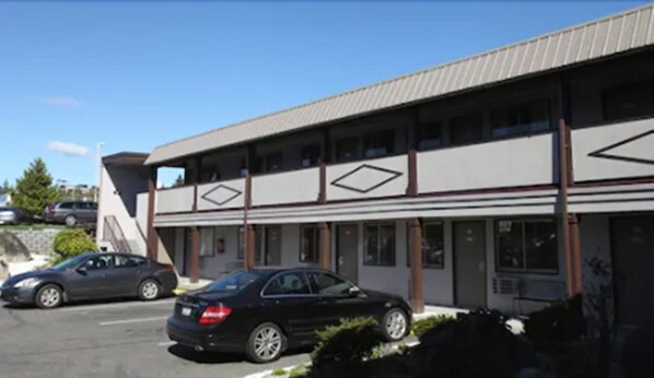 A two-story building with a flat roof and a series of windows on the ground floor. There are two cars parked in front of the building. - Seatac Inn (SeaTac)