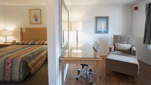 Habitación de hotel con cama, escritorio, silla, lámpara y un cuadro en la pared.