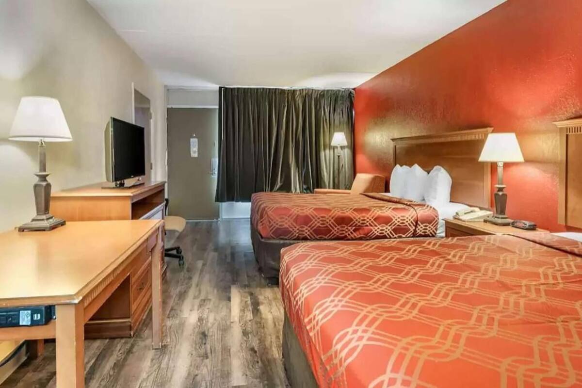 A hotel room with two beds, a desk, a TV, and a curtain.