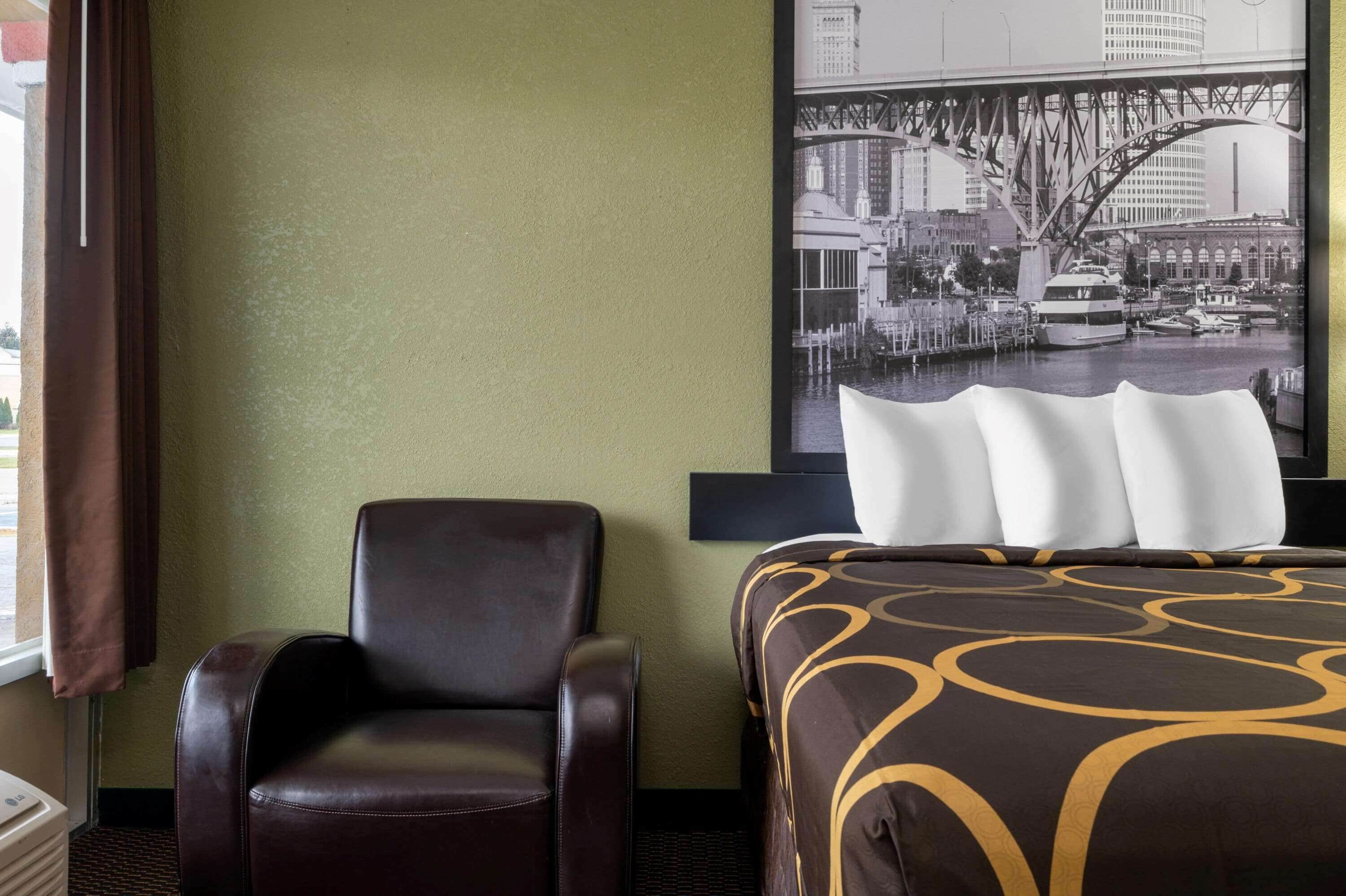 A hotel room with a bed, a chair, a large window, and a cityscape view.