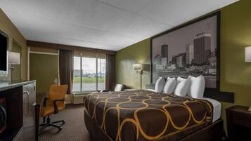 A hotel room with a large bed, a desk with a chair, a window with a cityscape view, and a mounted television.