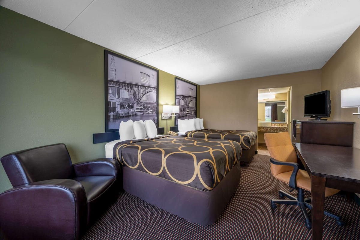 A hotel room with a large bed, two armchairs, a desk with a computer, and a television.