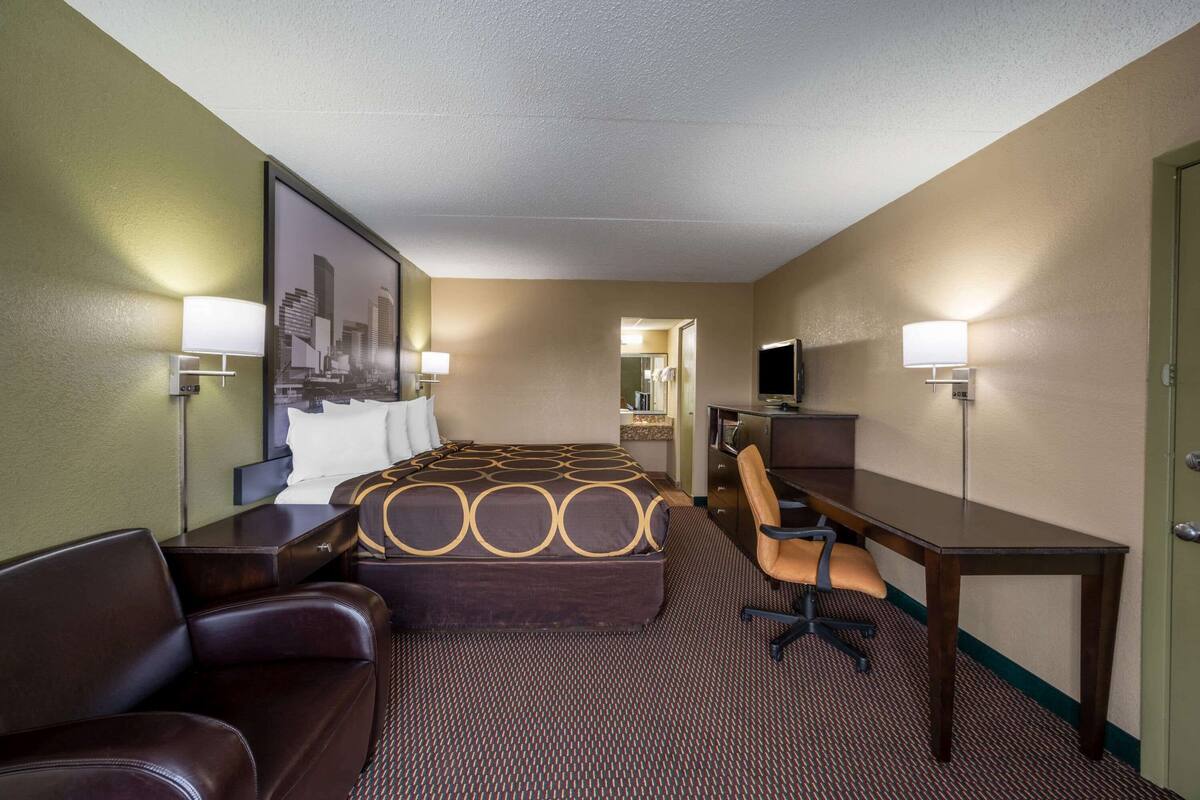A hotel room with a bed, a desk, a chair, a television, and a mirror.