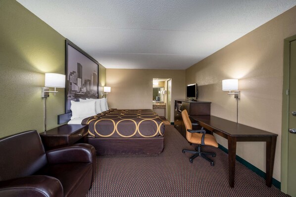 Quarto de hotel com cama, escrivaninha, cadeira, televisão e espelho.
