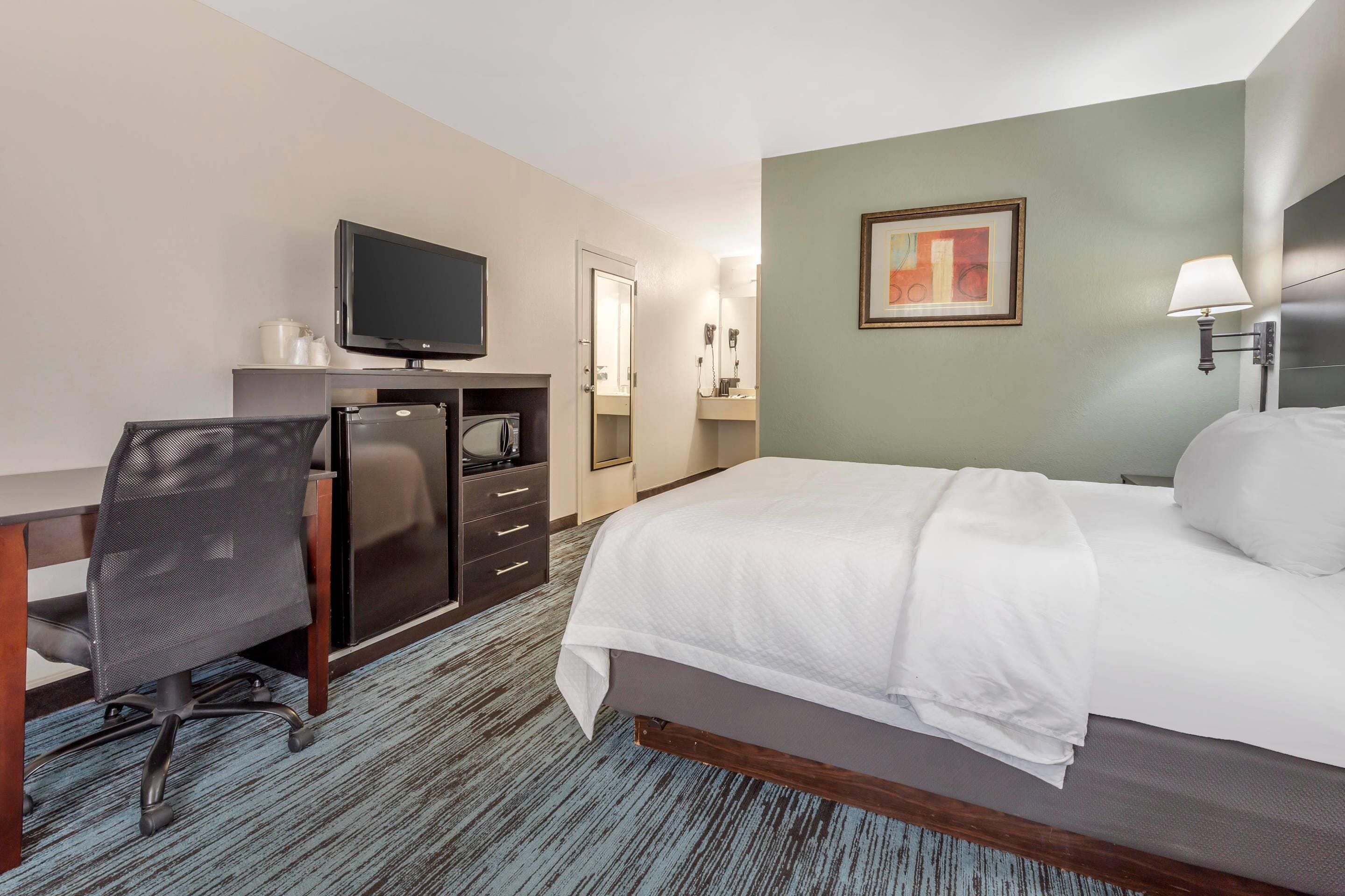 A hotel room with a bed, desk, chair, television, and a painting on the wall.