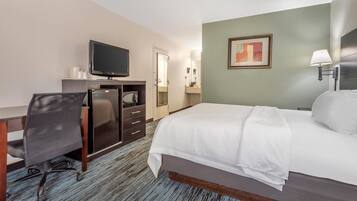 A hotel room with a bed, desk, chair, television, and a painting on the wall.