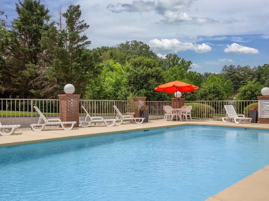 A swimming pool with white lounge chairs and an orange umbrella.