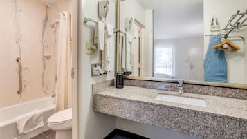 Un baño con bañera, inodoro, lavamanos de encimera de granito y espejo con toallero.