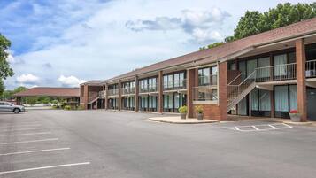 A multi-story motel with a parking lot, outdoor seating area, and a staircase leading to the upper floors.