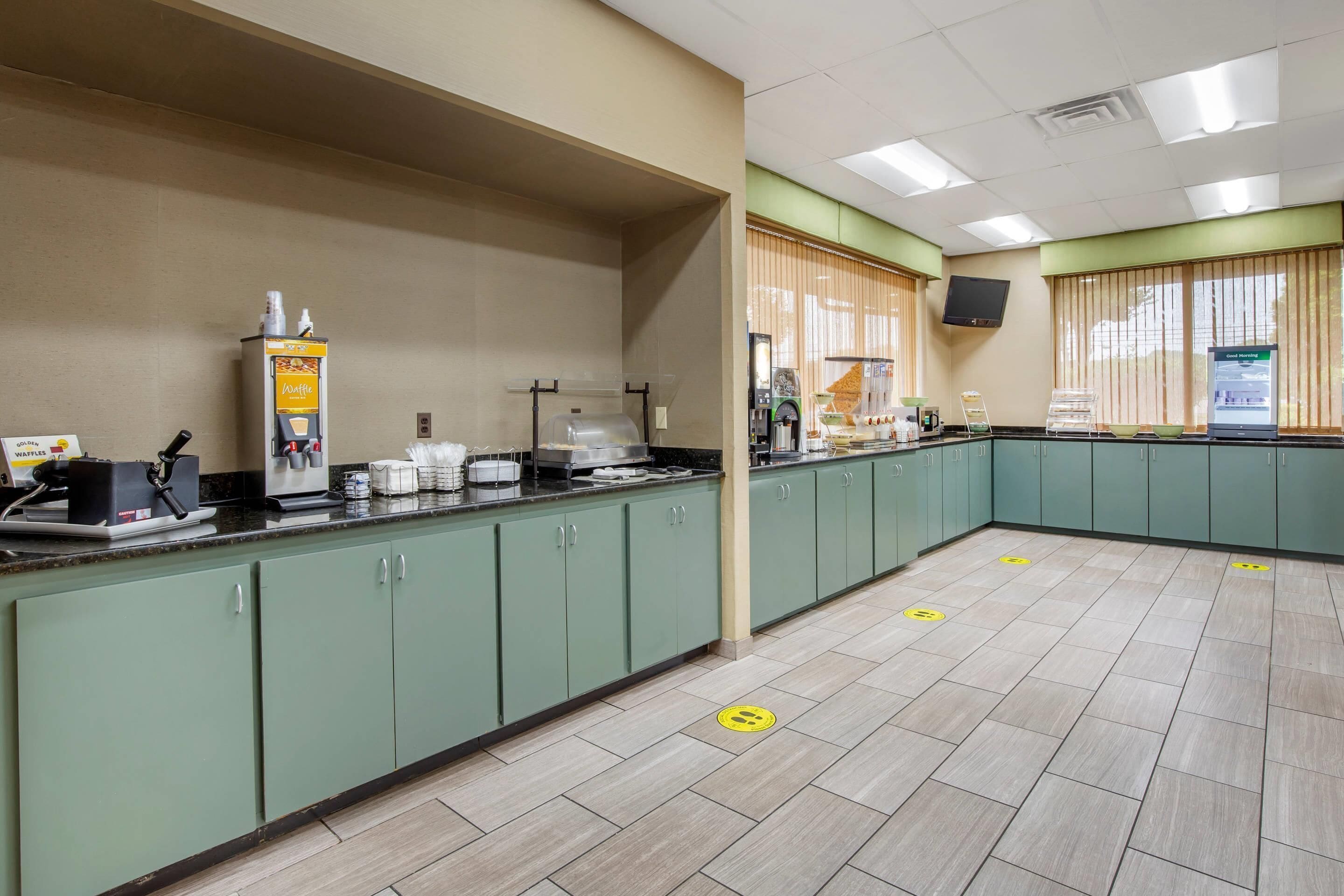 A spacious kitchen area with green cabinets, a coffee machine, a waffle maker, and a microwave.